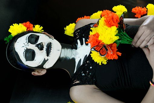 A girl with a skeleton make up holding a bouquet of orange and yellow flower