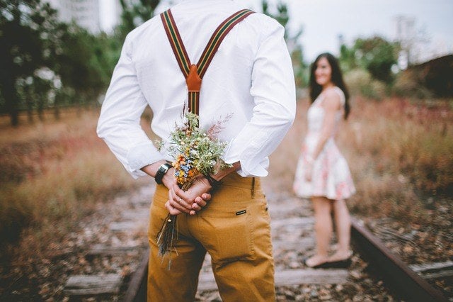 A boy holding a bouquet of flowers on his back to surprise his girlfriend