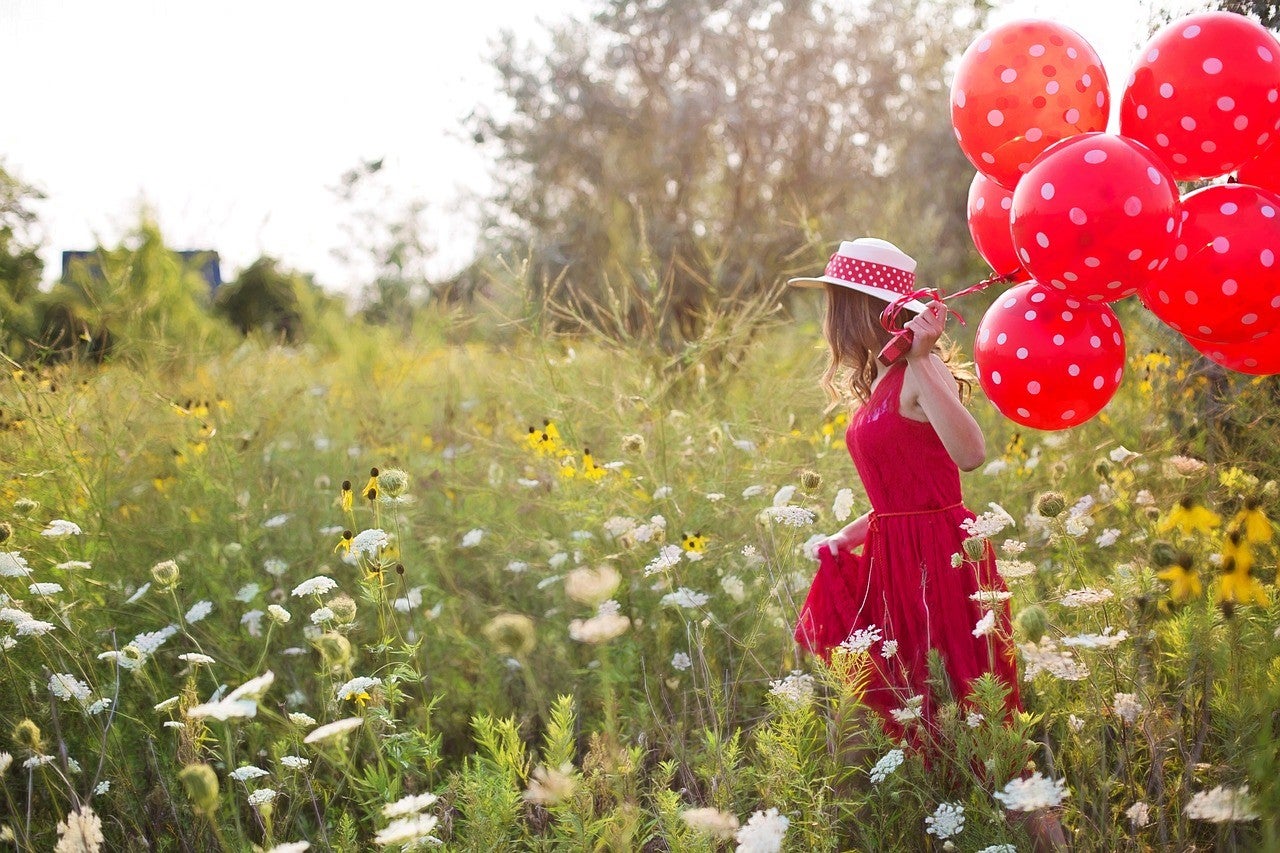 A woman wearing red dress and holding red dotted balloons