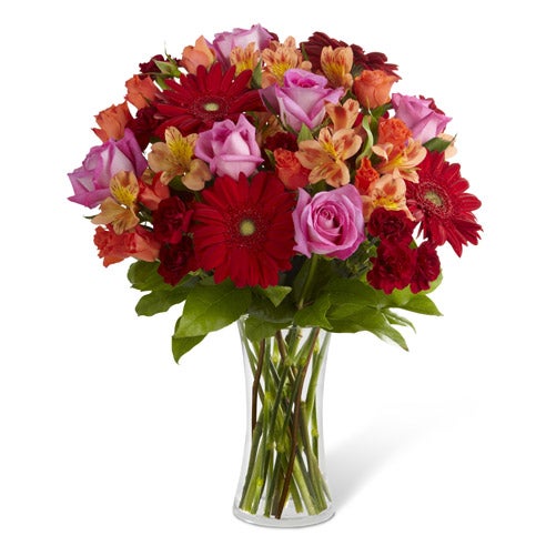 A Bouquet of Red Gerbera Daisy Flowers, Hot Pink Roses, Orange Spray Roses, Mini Burgundy Carnations and Peach Alstroemeria in a clear vase