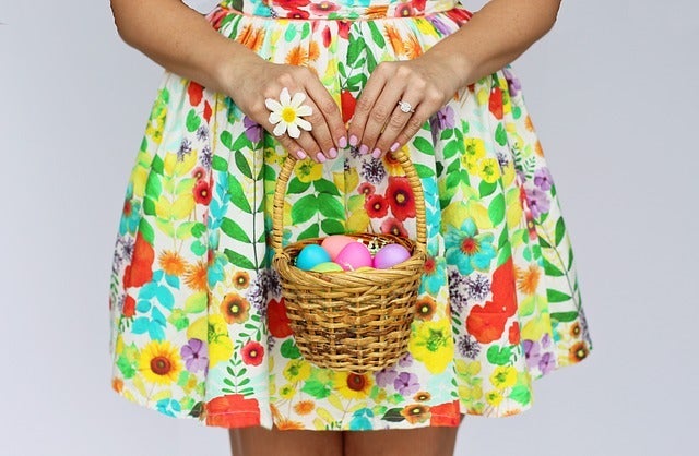 A girl wearing floral dress and a ring with flower design holding a basket with colorful easter eggs