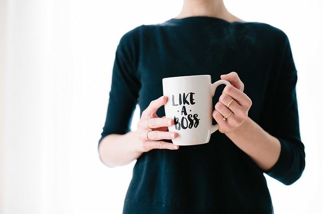 A woman wearing green sweatshirt and holding a mug with a print Like a  Boss