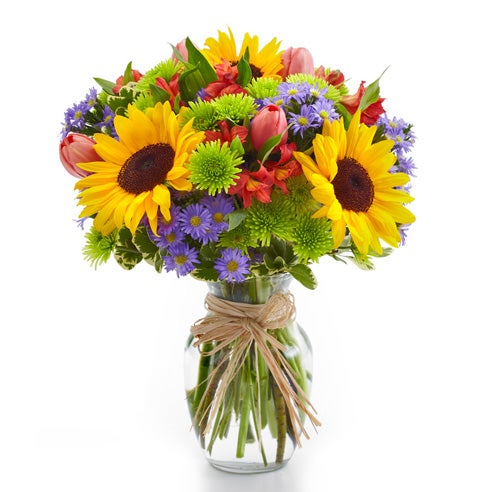 A glass vase of colorful bouquet including sunflowers, red tulips, green button poms,  monte casino, and purple alstroemeria