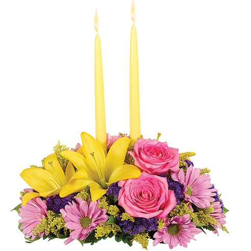 A Centerpiece flower arrangement including  Yellow Asiatic Lilies, Pink Roses, Blush Carnations, Lavender Daisy Poms, Purple Statice, Solidago, Leather leaf and Salal with  2 Yellow Candles