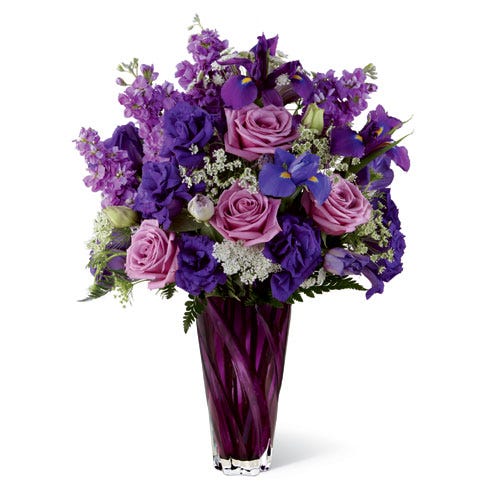 Purple roses are arranged with purple stock and blue iris