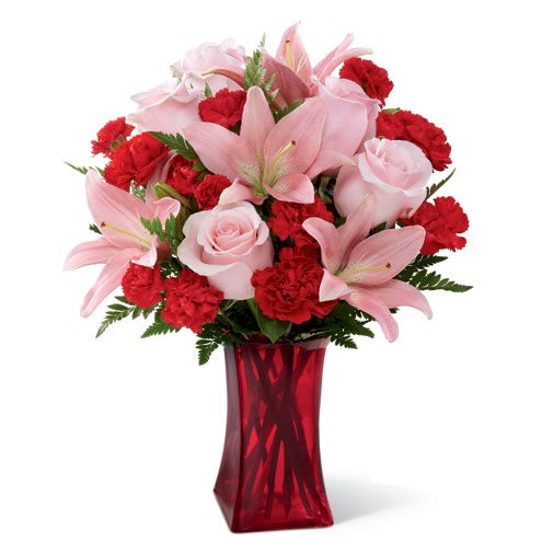 A Bouquet of  Pink Roses, Blush Asiatic Lilies, Red Carnations and Lush Greens in a Crimson Colored Glass Vase