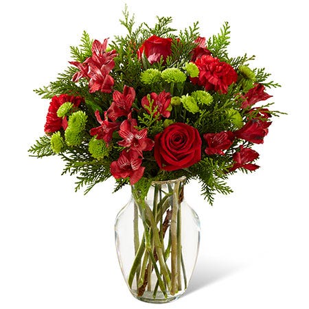 Christmas flower bouquet with red carnations, alstroemeria, evergreen stems and glass vase