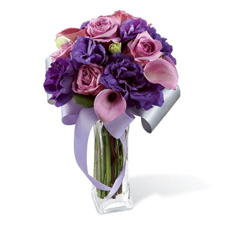 Lavender roses, lavender mini calla lilies, and deep purple double lisianthus in a clear glass flared square vase