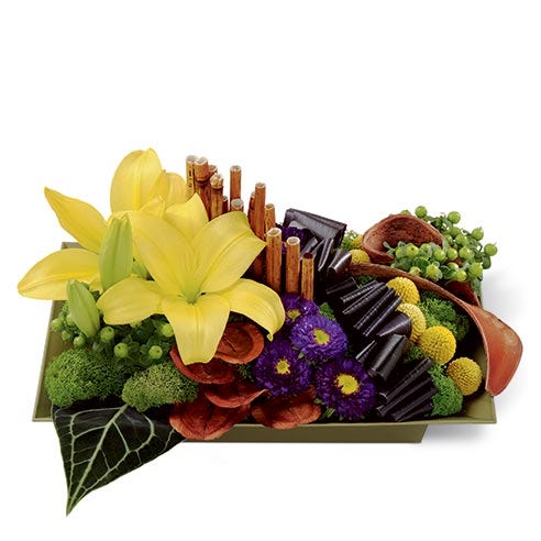Floral arrangement of yellow asiatic lilies, purple matsumoto asters, green hypericum berries, yellow craspedia, red ti leaves, anthurium leaves, dyed river cane stems, land lotus petals, and elephant ear pods