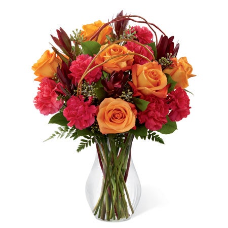 A Bouquet of Burnt Orange Roses, Fuchsia Carnations and Lush Greens with Curly Willow Branches in a Classic Clear Glass Vase