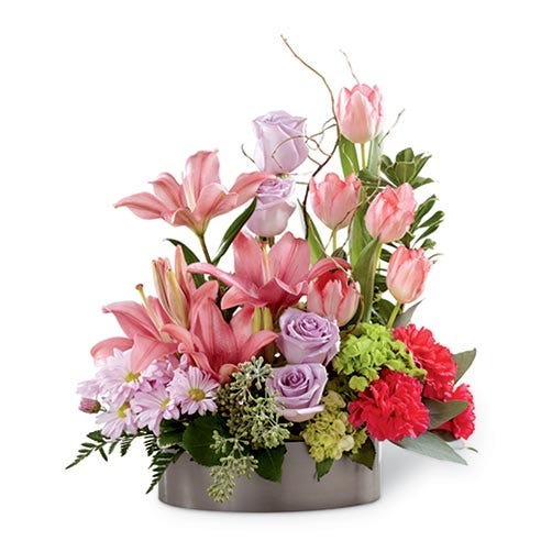 Lavender roses, pink tulips, fuchsia carnations, pink Asiatic lilies, lavender daisies, green mini hydrangea and an assortment of greens with curly willow tips in a metal oval container