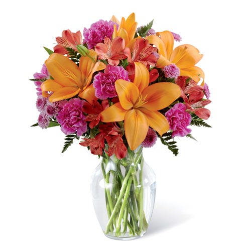 Orange lilies and pink carnations flower bouquet arrangement in a glass vase