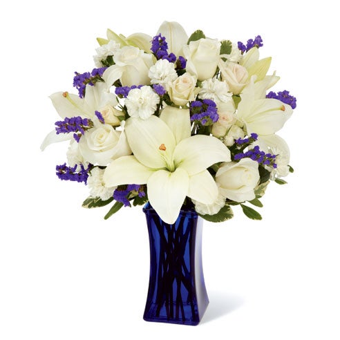 A Bouquet of White Asiatic Lilies, Pale Ivory Roses, Milky Mini Carnations, Blue Statice, Cream Spray Rose, and Lush Greens in a Dark Blue Glass Vase