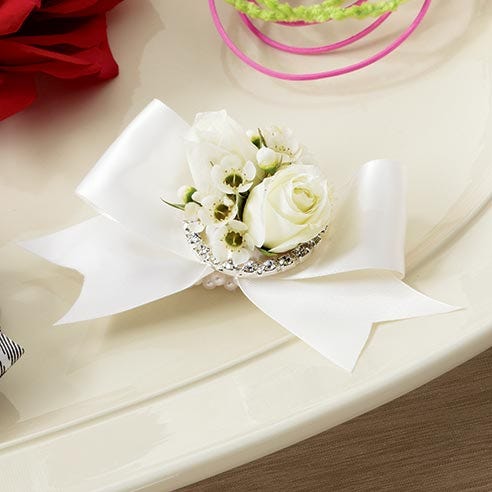 Wristlet with white spray roses and white waxflower brought together with an ivory satin ribbon