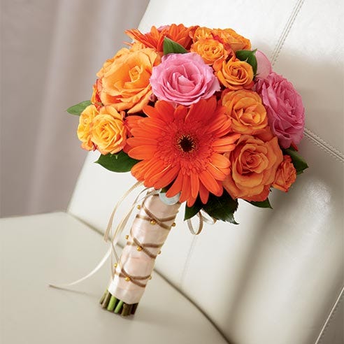 Tied bouquet of orange roses, spray roses, and gerbera daisies arranged with fuchsia roses all tied together at the stems with peach satin ribbon