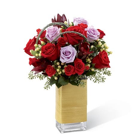 Red roses, lavender roses, red spray roses, white hypericum berries, and lush greens in a clear glass vase