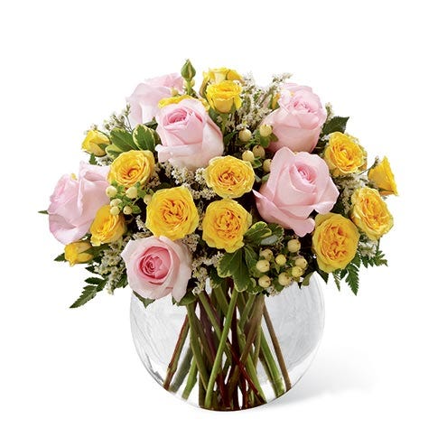 Pink roses, yellow spray roses, white hypericum berries, and white limonium in a clear glass bubble bowl vase
