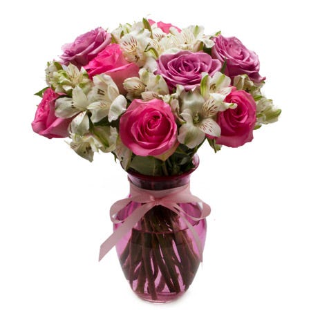 A Bouquet of Pink And Lavender Roses and White Alstroemeria in a Pink Glass Vase with a Pink Bow Decoration