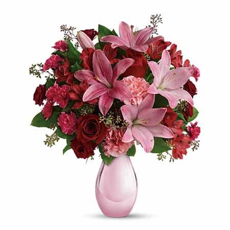 Pink lily, pink carnations, and red roses bouquet in a pink glass vase