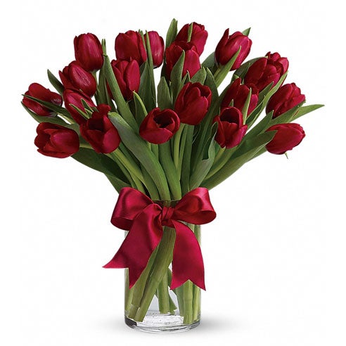 A bouquet of deep red tulips on a clear cylinder vase with a scarlet satin ribbon