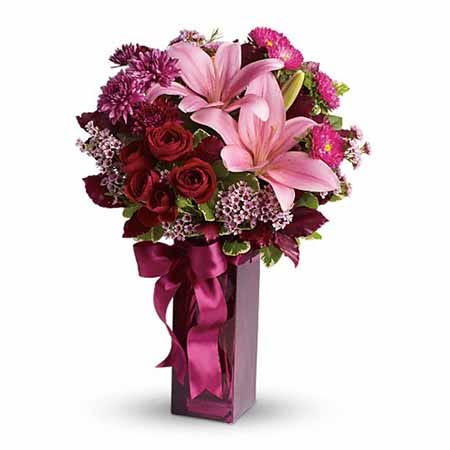 Dark pink lily and lavender wax flower bouquet in dark purple glass vase