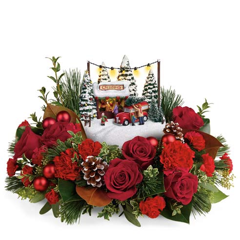 A centerpiece flower arrangement that includes Red Roses, Crimson Carnations, Mini Carnations, White Pine, Magnolia Leaves, Seeded Eucalyptus, Lemon Leaf, Oregonia, and Pinecones in a Mini Colored Ornaments with Kinkade's Family Tree Figure