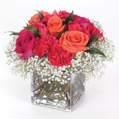 Hot pink roses, coral roses and red carnations in a modern square vase
