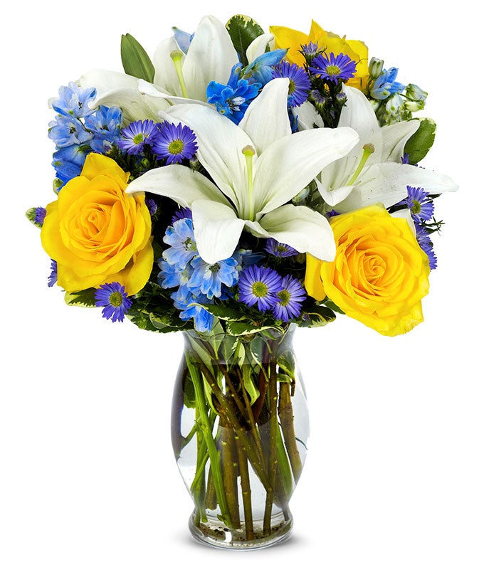 A bouquet of White Asiatic Lilies, Yellow Roses, Blue Delphinium and Purple Monte Casino on a glass vase