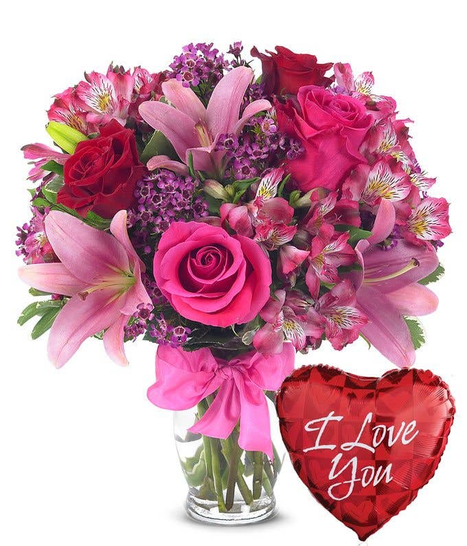 A Bouquet of Hot-Pink And Red Roses, Pink Asiatic Lilies, Blush Alstroemeria, and Indigo Waxflower in a Glass Vase With Bow with One Heart Themed Mylar Balloon