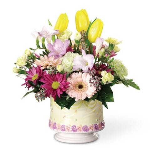 Yellow tulips, pink miniature gerbera daisies and light green carnations in a festive ceramic birthday cake container