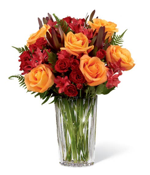 Orange rose and red Peruvian lilies with red spray roses in a crystal vase