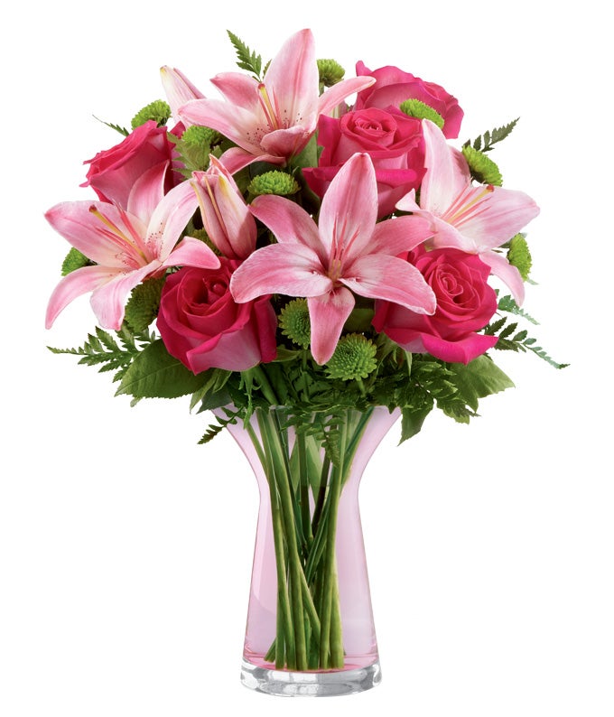 A bouquet of Pink Asiatic Lilies, Pink Roses, and Green Button Poms on a Pink Glass Vase