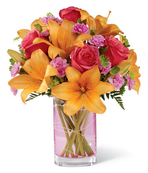 Floral arrangement in vibrant colors: peach roses, orange lilies, pink mini carnations in a pink hand-etched vase