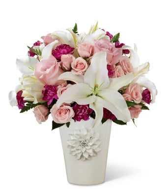 A bouquet of White Oriental lilies, Pink Spray Roses, Plum Mini Carnations and Lush Greens on a white ceramic vase