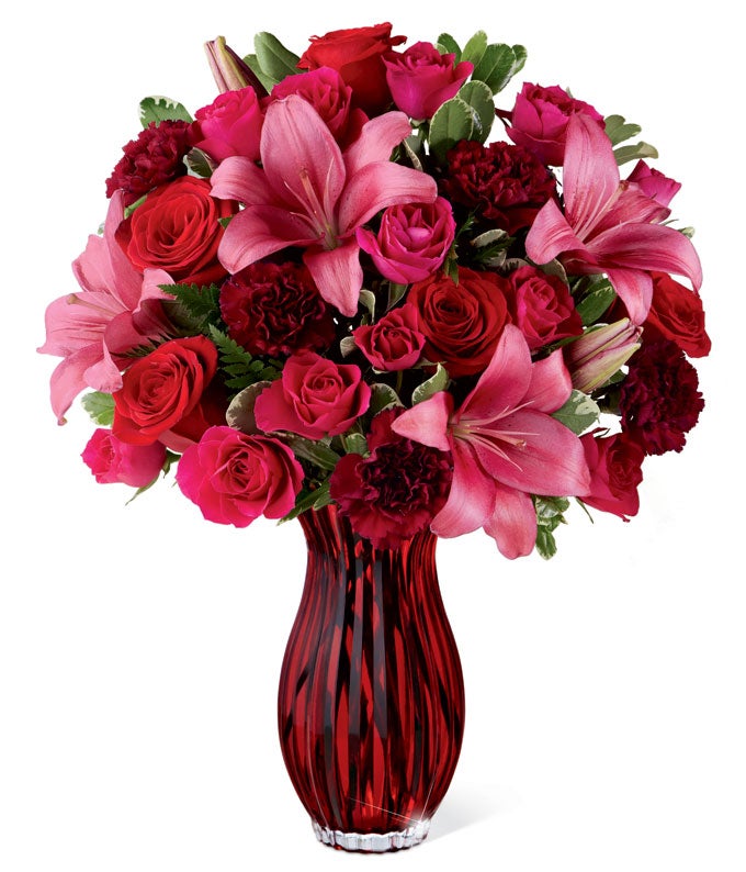 A bouquet of Dark Pink LA Hybrid Lilies, Red Roses, Hot Pink Spray Roses and Burgundy Carnations on a Sparkling Ruby-Colored Vas