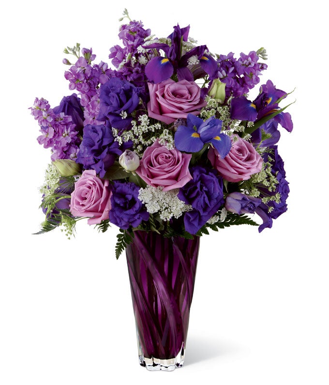 A Bouquet of Lavender Roses, Lavender Stock, Blue Iris and Lush Greens in a Purple Designer Vase