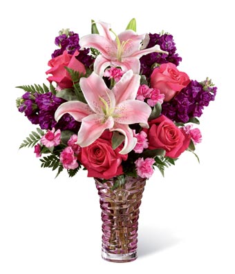 A bouquet of pink roses, stargazer pink lilies, mini pink carnations, purple stock and lush greens on a glass vase