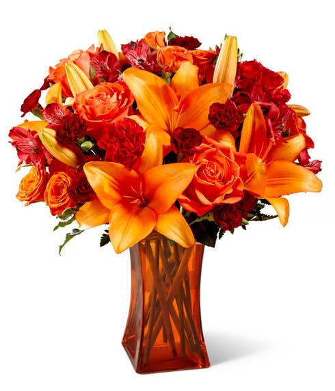 Dark orange roses and orange lilies bouquet inside a clear orange vase