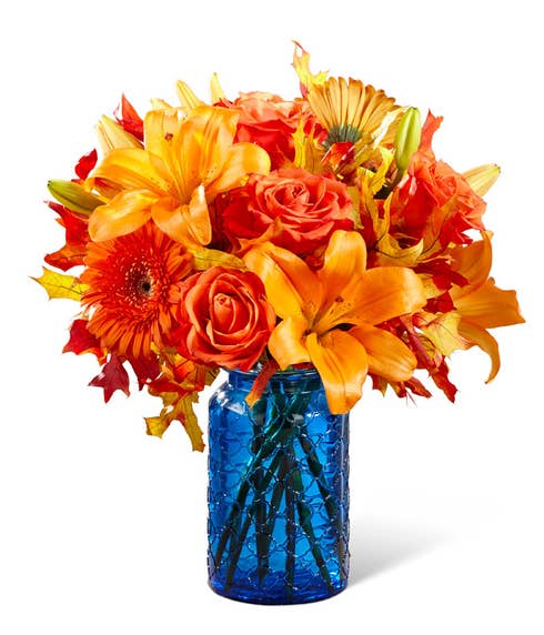 orange and blue flower bouquet with orange lilies, roses, and gerbera daisies in blue vase