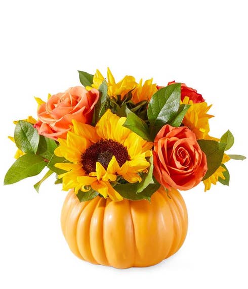 Yellow Sunflowers, Orange Roses, and green leaves in an orange ceramic pumpkin against a white background 