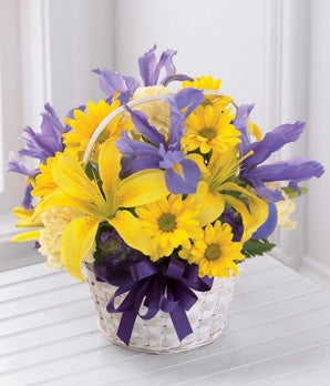 A Bouquet of Yellow Asiatic Lilies, Yellow Daisies, Pale Yellow Carnations, and Purple Iris in a White Washed Basket with Purple Ribbon