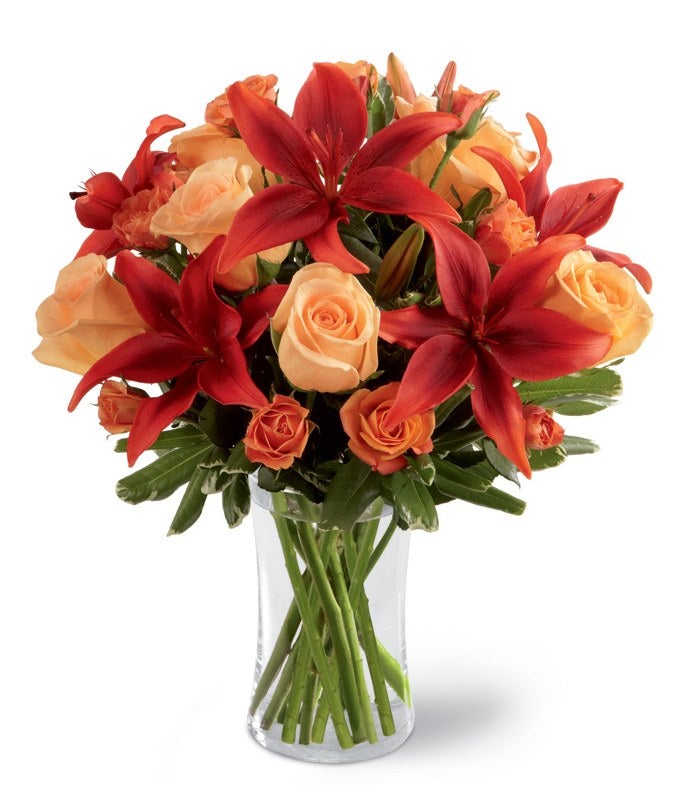 A Bouquet of Rustic Red Asiatic Lilies, Orange Spray Roses, and Seasonal Greens in a Clear Glass Vase with Card Message