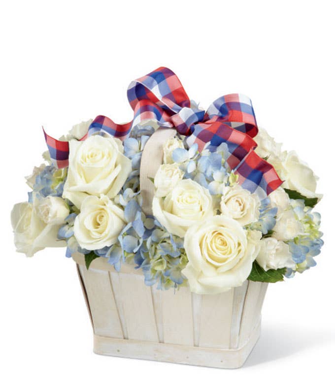 A Bouquet of  White Roses, White Spray Roses, and Blue Hydrangea in a White Washed Basket with Colorful Ribbon
