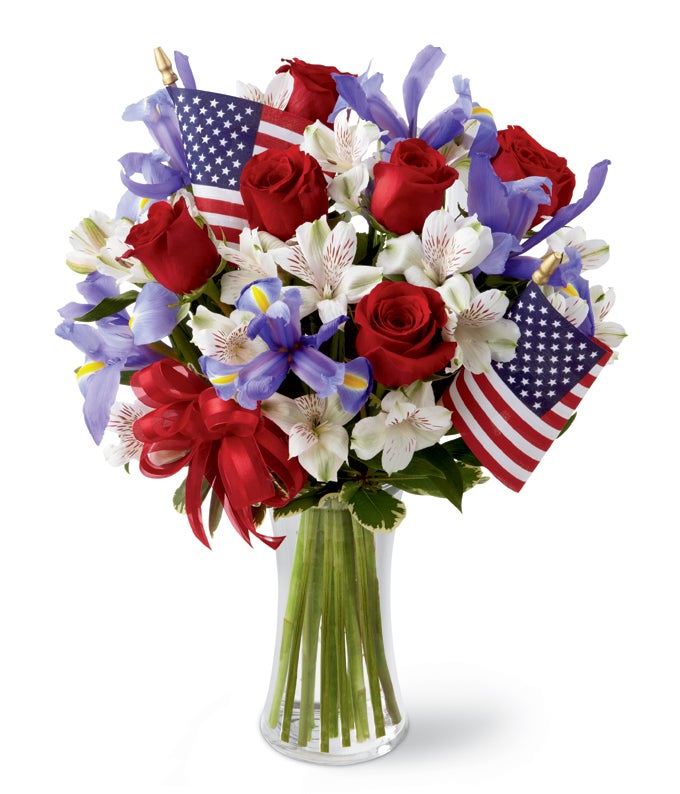A Bouquet of Red Roses, Blue Iris, White Alstroemeria, and Israeli Ruscus with Small America Flags in a Slender Gathering Vase