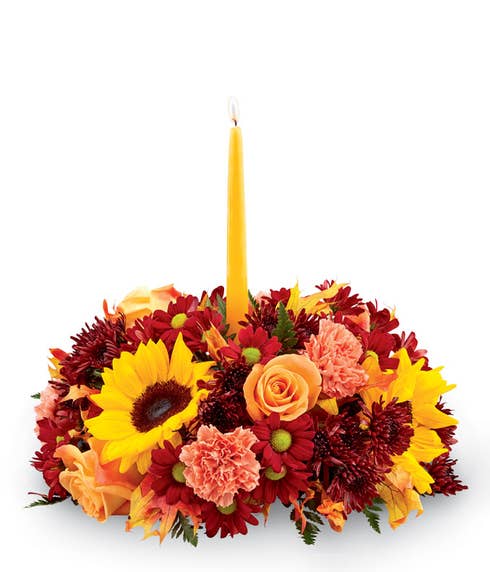 Fall floral centerpiece with sunflowers, orange roses and carnations and yellow candle