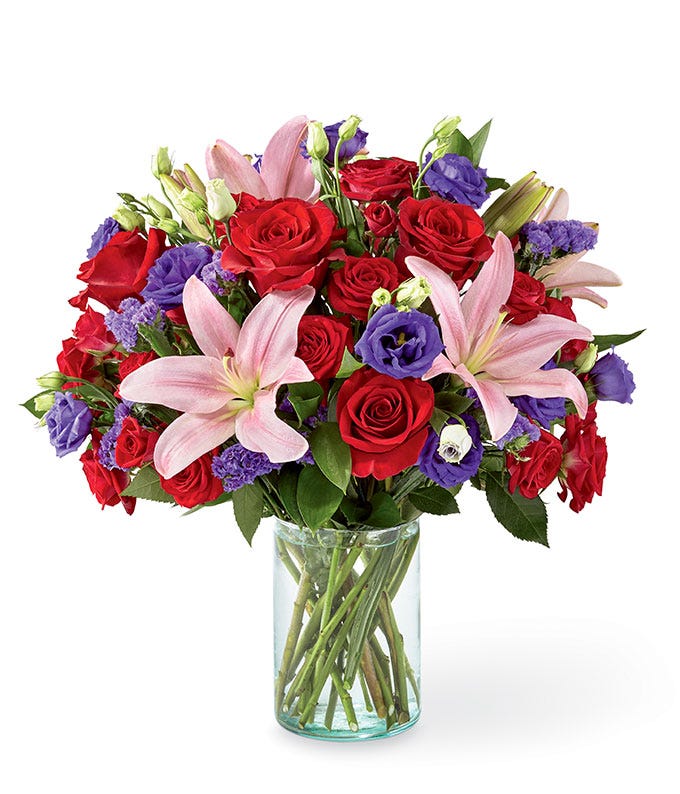Pink asiatic lily and red rose bouquet with purple statice in a glass vase