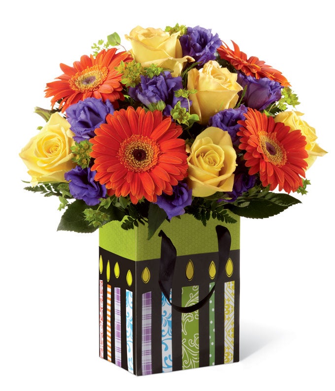 A Bouquet of Neon Orange Daisies, Yellow Roses, and Purple Lisianthus in a Birthday Gift Bag Container