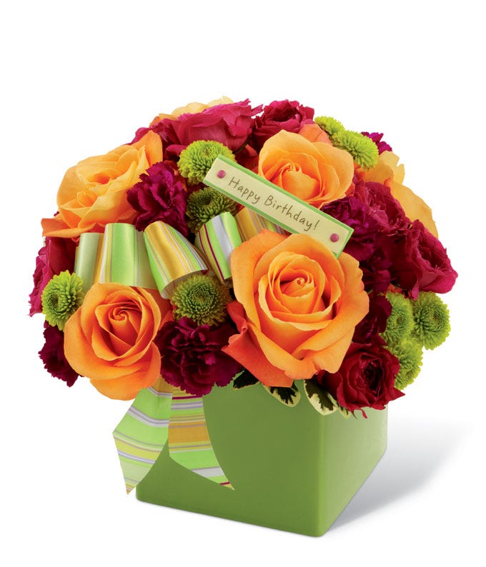 Orange roses, green button pompons and hot pink spray roses in unique green vase