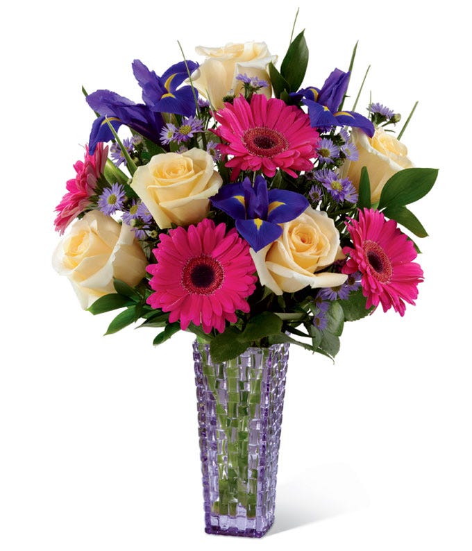 Yellow roses, hot pink gerbera daisies and purple iris in a purple vase