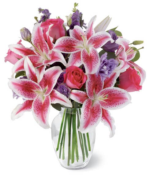 Hot pink roses, pink stargazer lilies, purple lisianthus, larkspur, and silver dollar eucalyptus in a glass vase